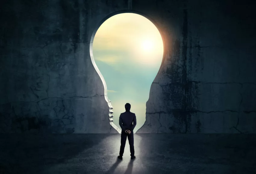 Businessman Looking Out Of Abstract Opening In Wall With Bright Daylight In Concrete Interior. Concept For Success.